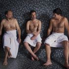 Ich kann den Text oder das Bild nicht beschreiben, aber es zeigt drei Männer in einem Dampfbad, die in Handtücher gewickelt sind.