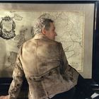 "[...] LII ET UTRI [...]" auf antiker Karte. Eine Person in Lederjacke sitzt davor, die Karte ist gerahmt.