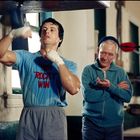 T-Shirt mit Aufschrift: "WIN 'ROCKY' WIN". Ein Mann trainiert am Boxsack, ein älterer Mann beobachtet ihn.