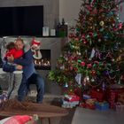 Links Karten auf Kamin, links Familie umarmt sich, rechts geschmückter Weihnachtsbaum, darunter Geschenke.