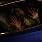 Ein erschrockener Mensch mit erhobenen Händen presst sich gegen eine Autoscheibe, eine Hand ist bandagiert. Es ist dunkel draußen.