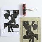 Abstrakte Druckgrafik mit schwarz-weißen Formen. Neben der Grafik liegt eine Walze und eine Druckplatte.