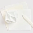 Blätter aus hellem Papier, teils mit goldenen Punkten, ein gefalteter Papieranhänger und ein weißer Stift aus Papier.