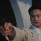 Ein Mann im weißen Anzug hält eine Waffe; sein Gesicht wirkt konzentriert und entschlossen.