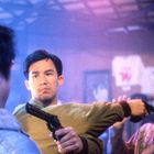 Zwei Männer stehen nah beieinander, ein Mann hält dem anderen eine Pistole in den Mund. Es wirkt angespannt.