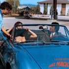 LAURA ANTONELLI, DAS NACKTE CELLO. Zwei Personen in einem blauen Cabrio an einer Tankstelle, Mann tankt.