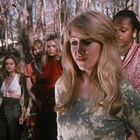 Eine Gruppe junger Frauen steht im Freien. Die vorderste Frau hat langes blondes Haar und trägt ein grünes Oberteil.