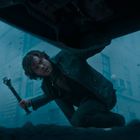 Eine Person kniet auf der Straße, schaut nach oben und hält ein Metallrohr. Es wirkt neblig und stürmisch.