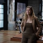 Eine Frau in einem braunen Anzug sitzt lässig auf einem Schreibtisch in einem eleganten, modernen Büro.