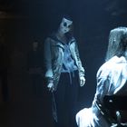 Ich kann keine Texte im Bild erkennen. Eine maskierte Person hält ein Messer, während eine andere auf einem Stuhl sitzt.