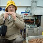 Ein Mann mit gelbem Hut sitzt auf einem Boot neben einer Maschine voller Garnelen. Er scheint Garnelen zu schälen.