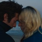 Ein Mann und eine Frau stehen Stirn an Stirn am Strand, im Hintergrund das Meer bei Dämmerung.