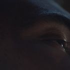 Kein Text vorhanden. Nahaufnahme eines Halbgesichts mit Fokus auf einem teilweise geöffneten Auge und dunkler Beleuchtung.