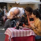 Eine fröhliche Szene in einem Straßencafé. "Casetta di Trastevere" steht auf einer Markise. Vier Personen sitzen entspannt.