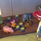 Mehrere Spielsachen, darunter ein rosa Sparschwein, Dinosaurier und ein Cowgirl, stehen auf einem Holzboden vor einem Schrank.