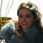 Eine Frau mit lockigem Haar und Haarklammern lächelt, während sie telefoniert. Im Hintergrund ist eine Pflanze.