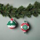 Zwei gehäkelte Weihnachtskugeln mit Schneeflockenmuster hängen an einem Tannenzweig.