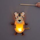 Eine handgehaltene Papierlaterne in Form eines lächelnden Tigers erhellt den Raum.