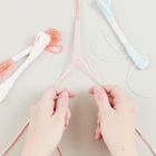 Person knotet ein Freundschaftsarmband mit rosa und weißen Fäden, umgeben von Garnstücken auf einem hellen Hintergrund.