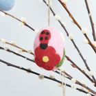 Ein Filz-Osterei mit roter Blume und gelber Mitte hängt an einem Zweig mit weißen Knospen.