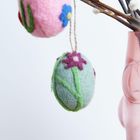 Filzkugeln mit Blumenmuster hängen an Zweigen in einer rosa Vase.