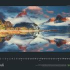 Text "Juli" und Kalendarium. Landschaft mit Bergen und See, Wolken und Bäume spiegeln sich im Wasser.