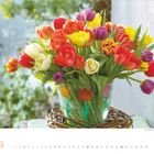 Tulpen. Kalender April 2027. Ein Strauß bunter Tulpen in einer Vase auf einem Tisch, umgeben von grünem Hintergrund.