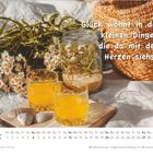 „Glück wohnt in den kleinen Dingen, die du mit dem Herzen siehst.“ Zwei Gläser Saft, Kamille, Muscheln, Buch.