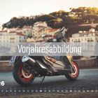 „Vorjahresabbildung“, „JUN 26“ mit Kalenderdarstellung. Ein Motorrad parkt vor malerischen Gebäuden und Bäumen.