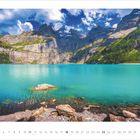 Kalender: Juli 2027. Ein klarer türkiser See mit Felsen am Ufer, umgeben von Bergen unter blauem Himmel mit Wolken.
