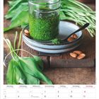 Kalender für April 2027 mit Wochentagen. Glas mit grünem Pesto, umgeben von Bärlauch und Mandeln.