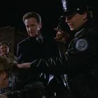 Ich kann den Text nicht entziffern. Eine Szene mit Polizisten, die einen Mann nahe eines Autos festhalten, bei Nacht.