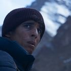 Ich kann den Inhalt nicht beschreiben, da kein Text zu erkennen ist. Ein Mann trägt eine Mütze vor einem schneebedeckten Berg.