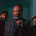 Drei Personen in dunkler Kleidung in einem Raum mit kühlem Licht, alle blicken ernst und direkt nach vorne.