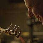 Ein Mann lächelt eine ausgestreckte Roboterhand an, umgeben von technischer Ausrüstung und warmem Licht.