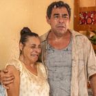 Zwei Personen, eine Frau und ein Mann, stehen nass unter einem Wasserstrahl in einem Wohnzimmer. Die Frau weint.