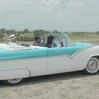 „Sunliner“ auf einem türkis-weißen Oldtimer-Cabrio, drei Personen fahren durch offene Landschaft.