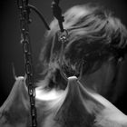 Keine erkennbaren Texte. Eine Person hängt mit Haken im Rücken, verbunden durch Seile und Ketten, düstere Stimmung.