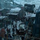 Im Hintergrund sind verschneite Berge sichtbar. Mehrere Zugwagons und Menschen bewegen sich in einer belebten Marktszene.