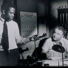 Ein Kalender zeigt September 1966. Zwei Männer, einer im Hemd, hält einen Telefonhörer. Hintergrund mit Gewehren.