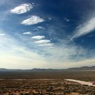 Keine Texte vorhanden. Weite Landschaft mit Hügeln im Hintergrund; ein einzelnes Auto auf einer staubigen Straße im Vordergrund.