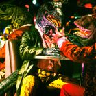 Illustration: Krokodilköpfige Figuren in bunter Kleidung sitzen an einem Tisch in einem clubähnlichen Umfeld.