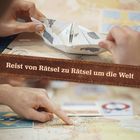 „Reist von Rätsel zu Rätsel um die Welt.“ Hände falten ein Origami, darunter zeigt ein Finger auf eine Landkarte.