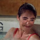 Text „VING“ auf weißem Kachelrand. Eine Frau in rotem Badeanzug lächelt im Wasser, Fliesenwand im Hintergrund.