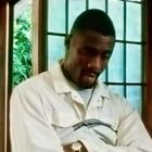 Keine Texte sichtbar. Ein nachdenklicher Mann in heller Kleidung steht vor einem Fenster mit Rautenmuster.