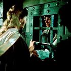 Eine Frau und ein Mann schauen sich durch ein vergittertes Fenster an, der Mann hält ein Stück Papier.