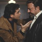 Zwei Männer stehen nah beieinander, einer gestikuliert intensiv mit der Hand, beide tragen Mäntel, ernste Stimmung.