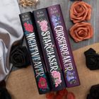 "NIGHTRENDER," "STARCHASER," "CURSEBREAKER." Buchrücken mit floralen Motiven, umgeben von Stoff und Rosen.