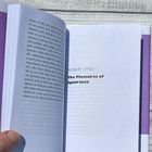 Text: "How glad I am I need not hurry." Ein Buch mit lila Rückseite, auf hellem Holzhintergrund liegend.