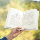 "51 Opening Our Eyes to Modern Miracles" steht oben auf einer Buchseite. Eine Hand hält das Buch vor einem unscharfen, grünen Hintergrund.